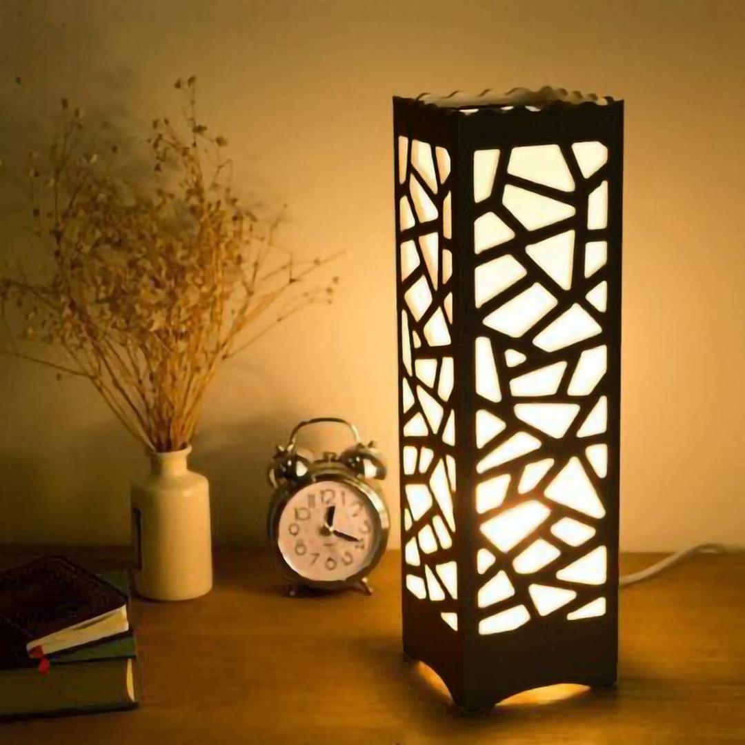 Modern geometric table lamp glowing on a wooden desk with clock, books, and dried flowers