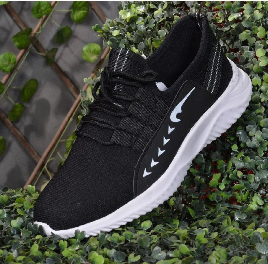 Black athletic sneaker with white sole and arrow accents, displayed on green foliage