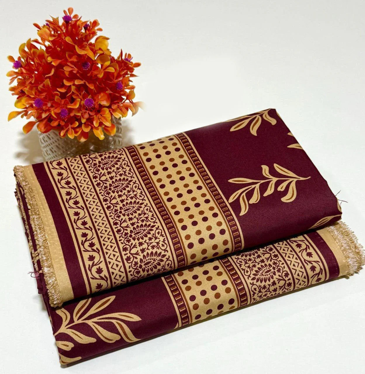 Maroon and beige cotton 2-piece unstitched suit with floral and dot patterns, next to orange flowers