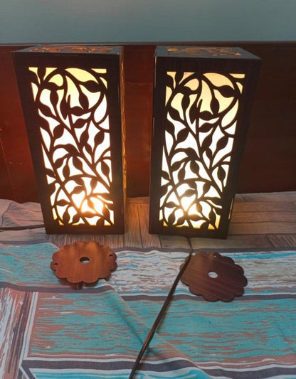 Pair of wooden table lamps with leaf cut-out design on a patterned bedsheet