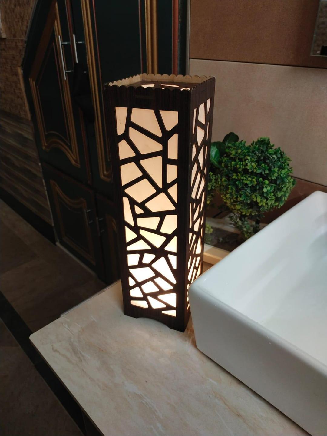 Modern geometric table lamp with warm light on bathroom countertop next to a green plant