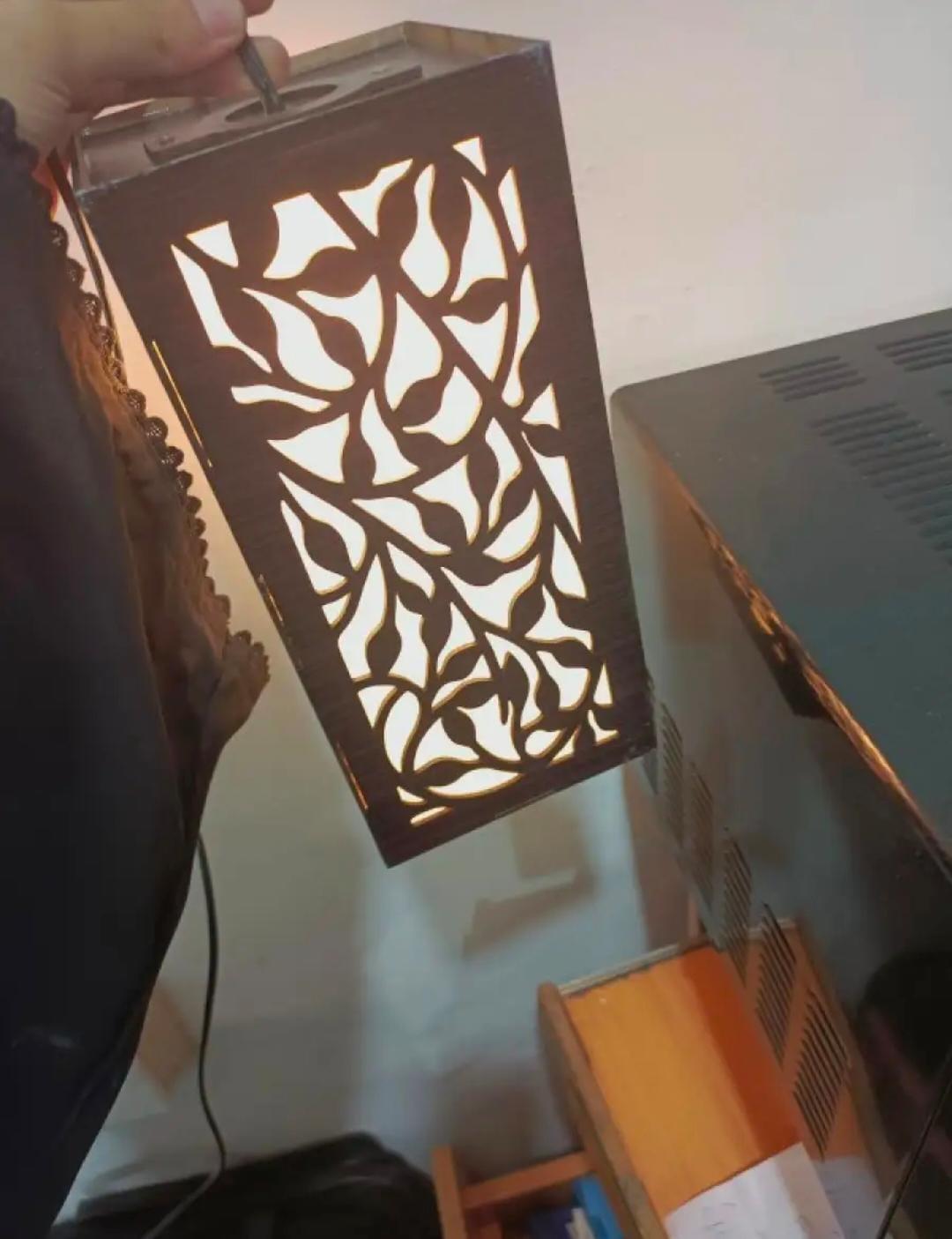 Hand holding decorative wooden lamp with leaf pattern cutouts, glowing indoors
