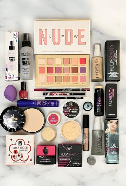 Flat lay of assorted makeup products including Huda Beauty eyeshadow palette, foundation, primer, Miss Rose makeup fixer spray, powders, brushes, and cosmetic tools on a marble background.