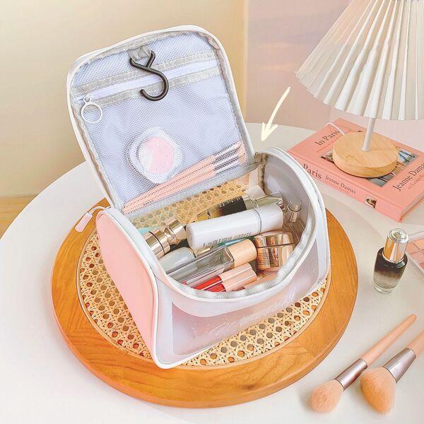 Open pink travel makeup bag with cosmetics on vanity table beside lamp and brushes
