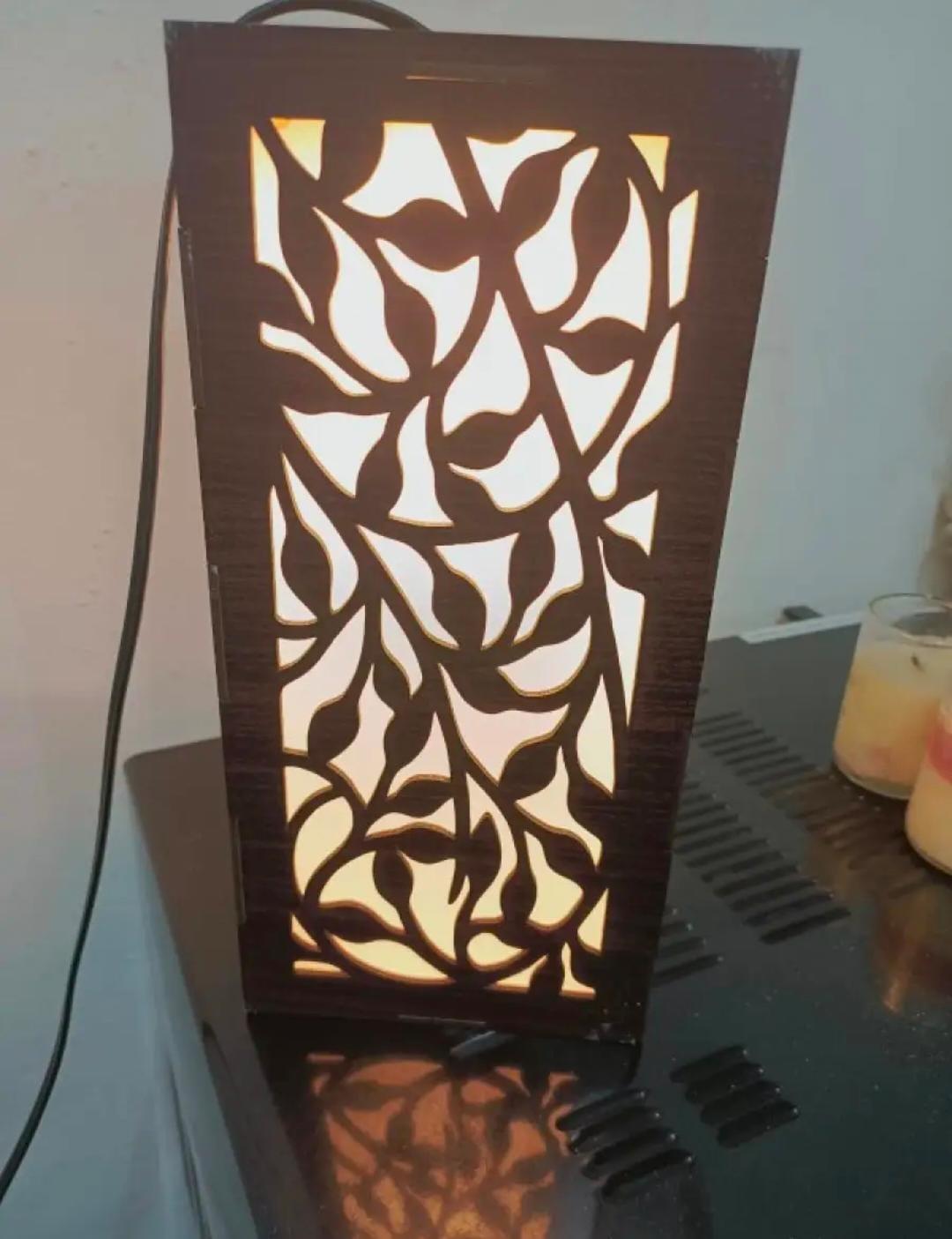 Decorative wooden table lamp with intricate leaf cutout design and warm backlighting