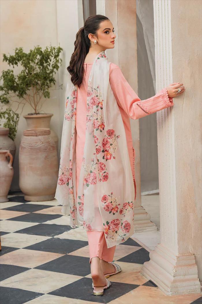 Woman in peach floral Pakistani suit with chiffon dupatta, standing in elegant courtyard