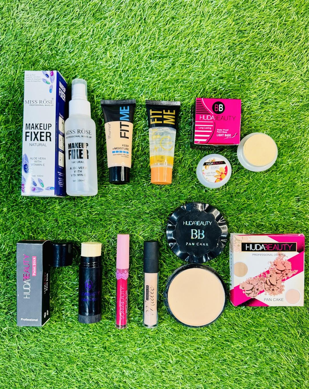 Assorted makeup products including Miss Rose, Fit Me, and Huda Beauty on green grass
