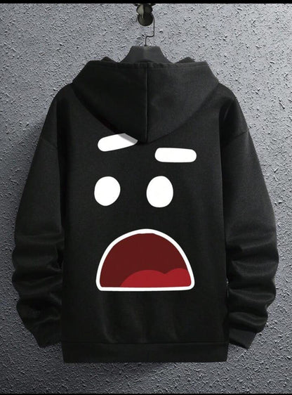 Black hoodie with surprised cartoon face graphic on the back, hanging on textured wall.