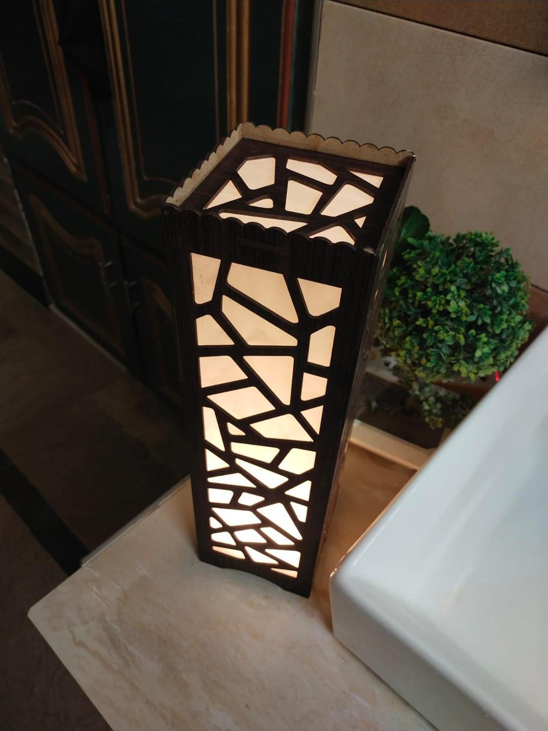 Modern geometric wooden table lamp with warm light beside a bathroom sink and small plant